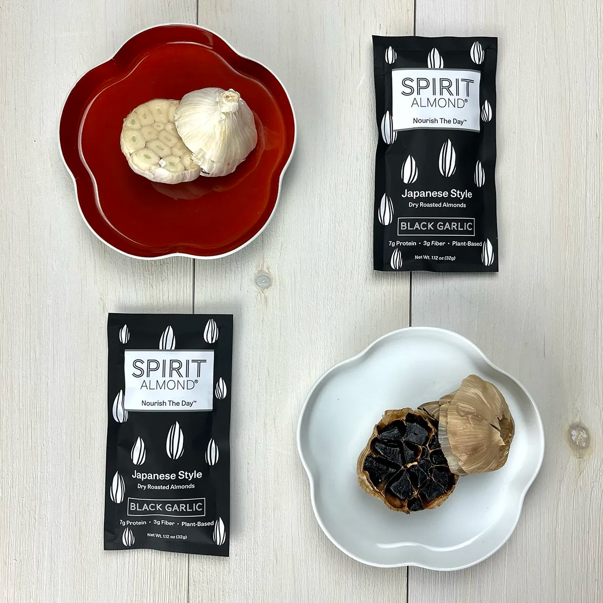 Cross section of white garlic and black garlic with two packages of SPIRIT Almond Black Garlic Almonds