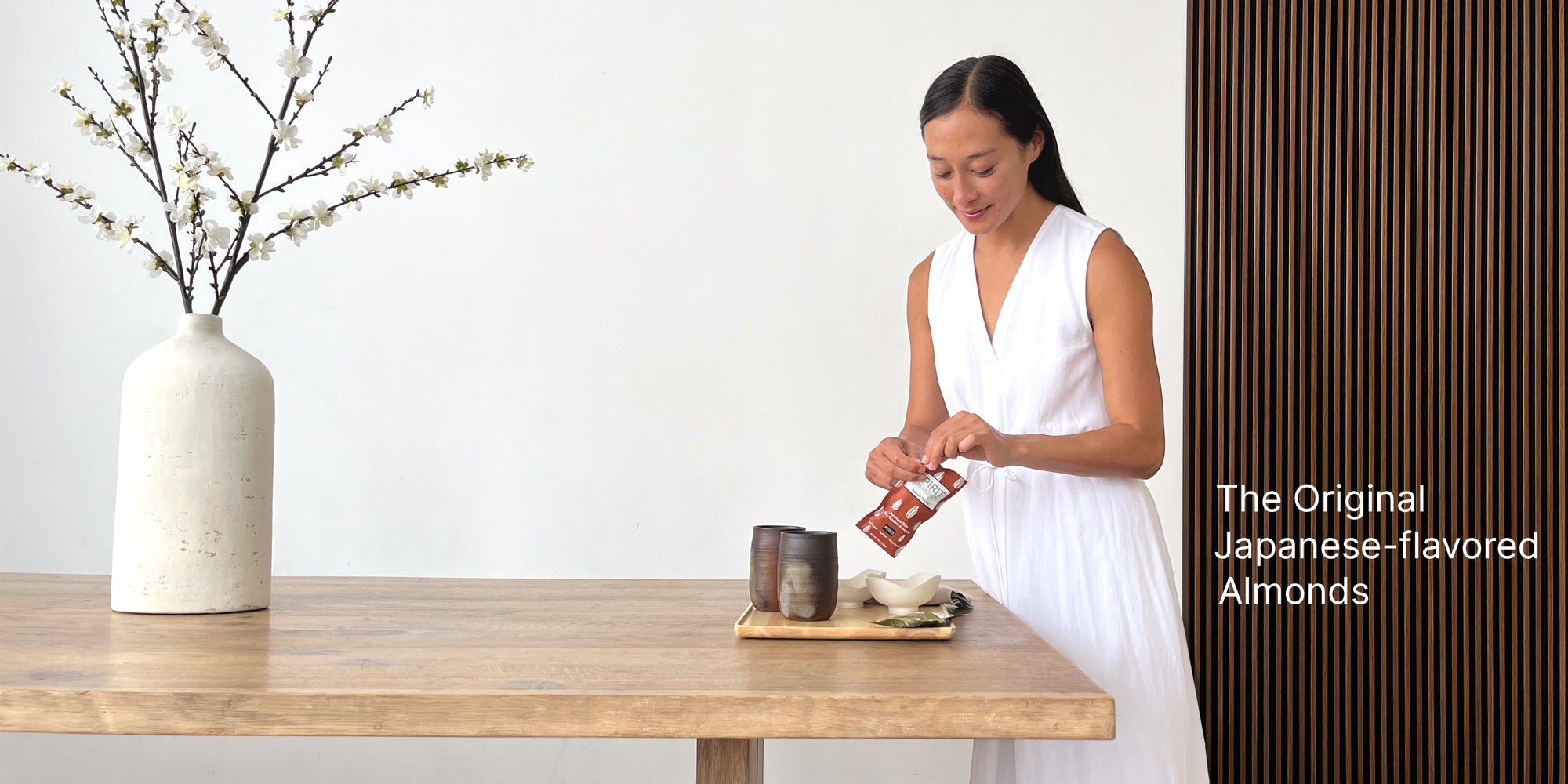 Woman opening a package of SPIRIT Almond in a minimalist Japanese room. Titles: "The Original Japanese-flavored Almonds"