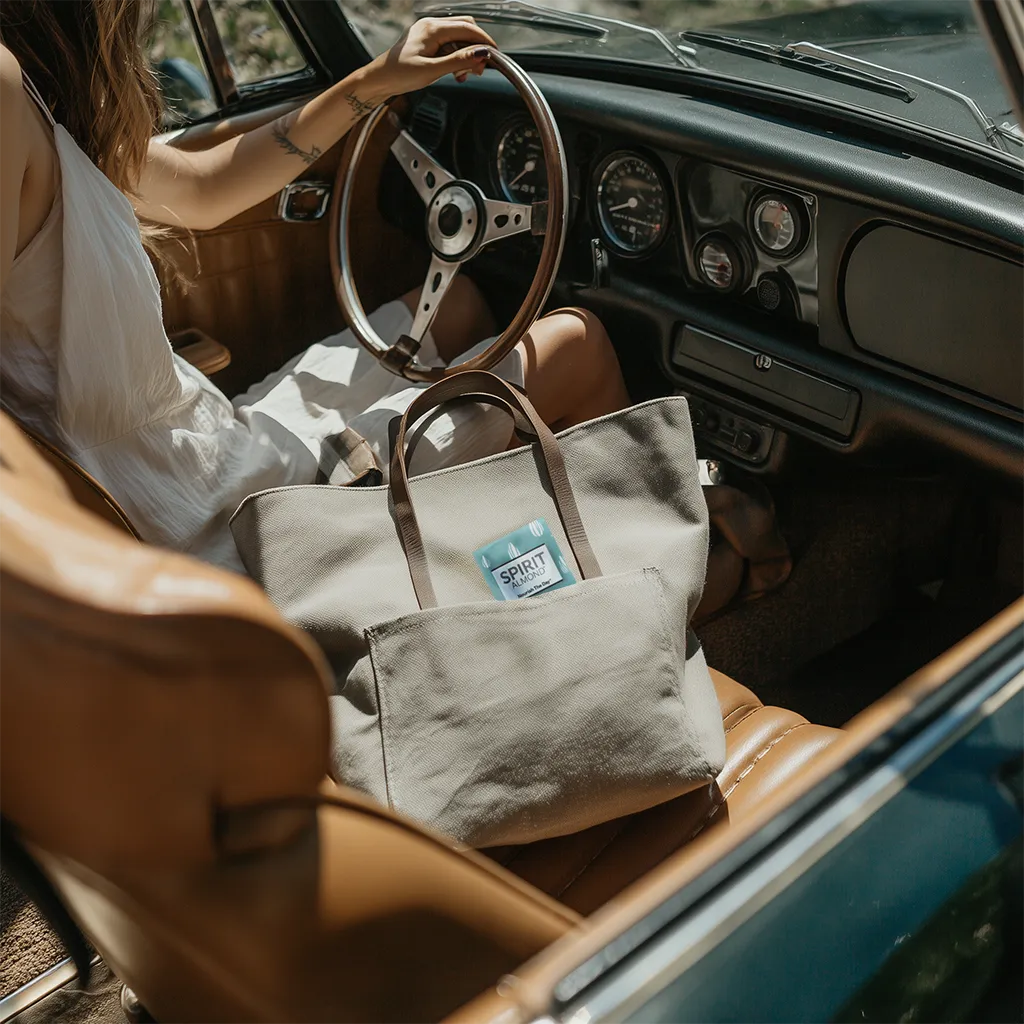 Person sitting in a vintage car next to a gray tote bag. A package of SPIRIT Almond is sticking out of the pocket