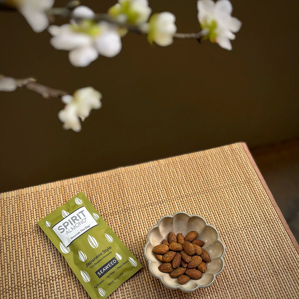 SPIRIT Almond Seaweed package, next to dish of almonds, sitting below a flowering tree.