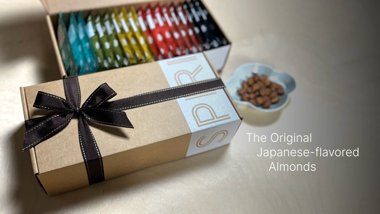 Gift Box of SPIRIT Almond with tied ribbon, open box display showing colorful packaging, and plate of almonds