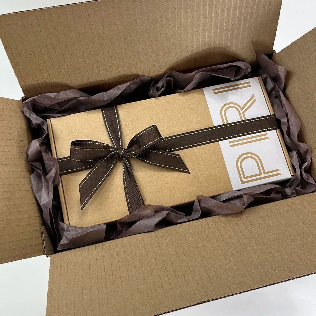 SPIRIT Almond Double Gift box with tied stitched ribbon surrounded by tissue paper in an open shipping box