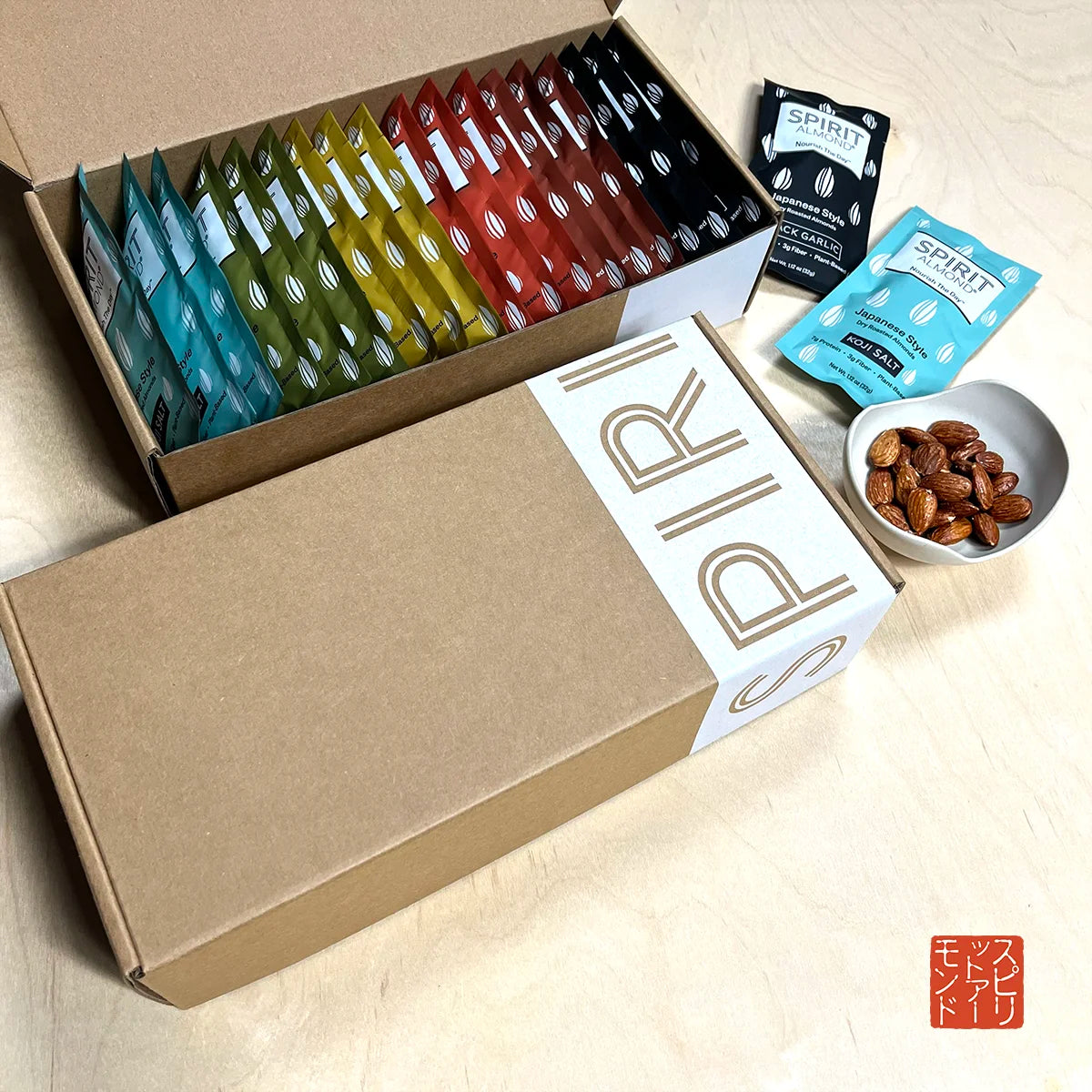 SPIRIT Almond Japanese Style Dry Roasted Almonds Gift Box in colorful lineup, six flavors. Koji Salt, light blue. Seaweed, green. Mustard, yellow. Curry, reddish orange. Miso, brownish-red. Black Garlic, black. Dish of almonds.